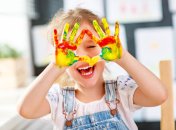 funny child girl draws laughing shows hands dirty with paint