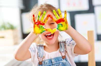 funny child girl draws laughing shows hands dirty with paint