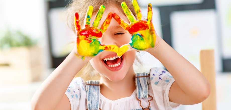 funny child girl draws laughing shows hands dirty with paint