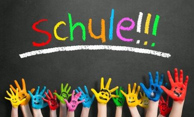 viele angemalte Kinderhände mit Smileys vor Kreidetafel mit dem Wort "Schule"