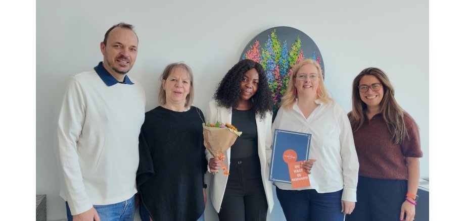 „Eine pädagogische Fachkraft aus Namibia erhält im Beisein von Verwaltungsvertreterinnen ihre Anerkennungsurkunde im Rahmen einer feierlichen Veranstaltung.